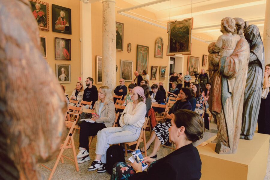 dziennikarze i przedstawiciele placówek muzealnych siedzą na krzesłach i słuchają konferencji